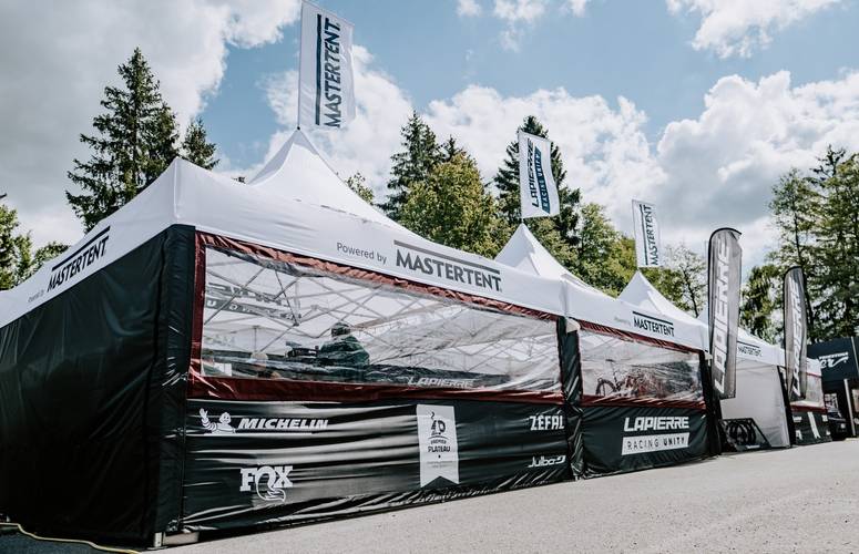 Lapierre Racing Unity Faltzelt 5x5m von Mastertent Ein weiß-schwarz bedrucktes 5x5m Faltzelt von Mastertent für das Lapierre Racing Unity Team mit geschlossenen Seitenwänden, Klarsichtfenstern und Sponsoren-Logos wie Michelin und Fox im Außenbereich.