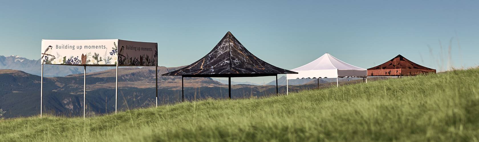 Mastertent Faltpavillons Die verschiedenen Modelle von Mastertent Faltpavillons stehen vor einer Bergkulisse.