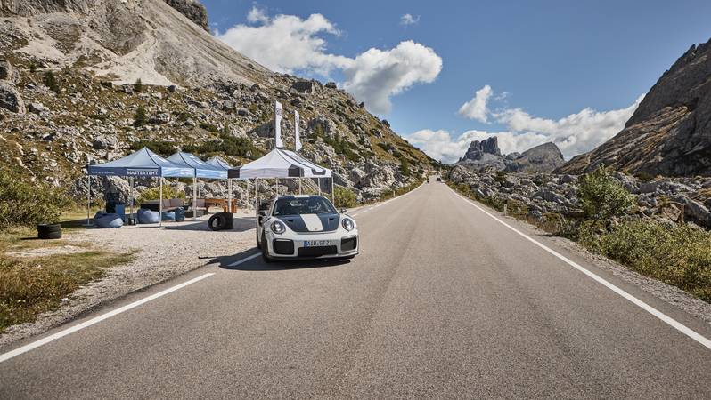Faltpavillons mit Sportauto Neben einer Straße stehen drei blaue und ein weißer Faltpavillon mit schwarzem Aufdruck. Auf der Straße ist ein Auto zu sehen.