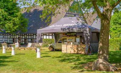Mastertent Catering-Zelt für Luises Weinbar in Bielefeld Mobiles Weincatering im Freien: Ein graues Mastertent Faltzelt für „Luises Weinbar“ mit Verkaufs-Theke, Liegestühlen und Stehtischen vor einer historischen Fachwerkscheune.
