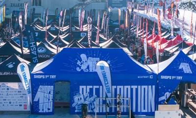 Ecotent Eventzelte beim „Shops 1st Try“ im Skigebiet Drohnenaufnahme vom Snowboard-Event „Shops 1st Try“ mit großen, blau bedruckten Ecotent und Mastertent Eventzelten (8x4m und 4x4m), passenden Beachflags und geschlossenen Seitenwänden im Schnee vor dem Zillertal Shuttle.